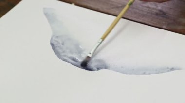 Erkek ressamın yakın çekimi soyut bir resim çizer, ıslak tuvale birkaç damla siyah boya döker ve boya fırçasıyla onu dağıtır.