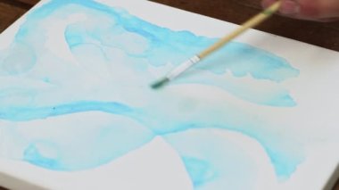 Sıvı Sanat. Soyut renkli tablolar. Kadın ressamlar tuvale mavi şekilli su dağıtmak için boya fırçası kullanır.