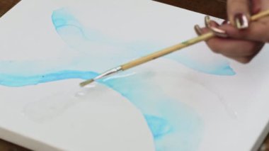 Sıvı Sanat. Soyut renkli tablolar. Kadın ressamlar tuvale mavi şekilli su dağıtmak için boya fırçası kullanır.