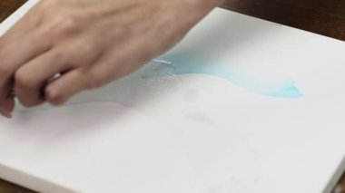 Ressamın yakın çekimleri soyut bir resim çizer. Islak tuvale mavi boya ile soyut şekiller çizer.