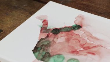 Sıvı Sanat. Soyut renkli tablolar. Kadın ressamlara yakın çekim kırmızı ve yeşil boyalarla tuvale su döker.