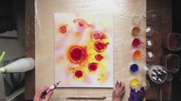 Vista superior do artista masculino pinta uma imagem abstrata, ele derrama um monte de algumas gotas de tintas vermelhas e pretas para tela molhada — Vídeo de Stock