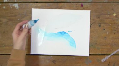 Kadın ressamın üst görüntüsü güzel soyut şekiller çizer, ıslak tuval üzerine mavi boya döker.