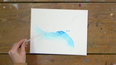 Sıvı Sanat. Soyut renkli tablolar. Kadın ressamın üst görünümü, pipetten tuvale mavi soyut resimli su döker