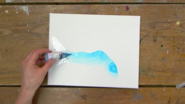 Erkek ressamın üstten görünüşü güzel, soyut bir tablo çiziyor, ıslak tuval üzerine mavi boya döküyor.