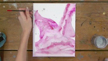 Sıvı Sanat. Soyut pembe resim. Kadın ressamın üst görünümü soyut bir resim çizmek için boya fırçası ve gümüş boya kullanır