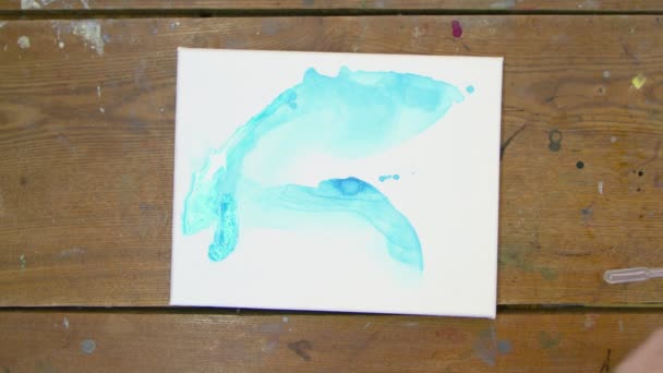 Top view női kéz művész festi gyönyörű absztrakt képet, ő önti kék festék cső nedves vászonra, és használja festőecset szétosztani — Stock videók