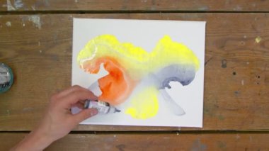 Sıvı Sanat. Soyut renkli tablolar. Erkek ressamın üst görüntüsü, turuncu ve sarı renklerle ıslak tuvale siyah boya döküyor.