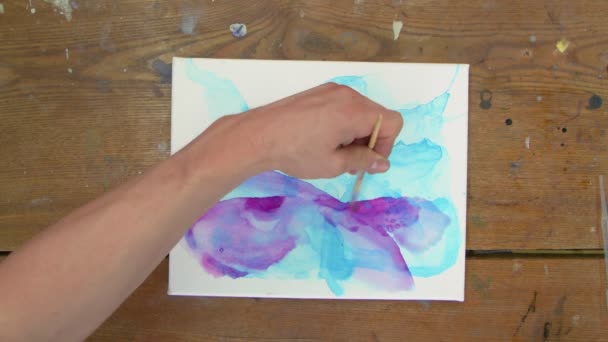 Vista dall'alto dell'artista dipinge un quadro astratto, usa pennello per dipingere forme astratte con vernice viola su tela bagnata — Video Stock