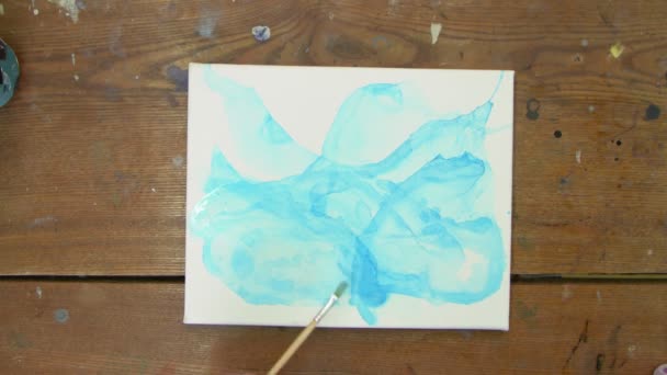 Ressamın üst görüntüsü soyut bir resim çizer, mavi bir resim üzerinde suyla boya fırçası kullanır. — Stok video