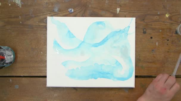 Arte Fluida. Pintura azul abstrata. Vista superior do artista feminino derrama água da pipeta para a tela e usa pincel para distribuí-lo — Vídeo de Stock