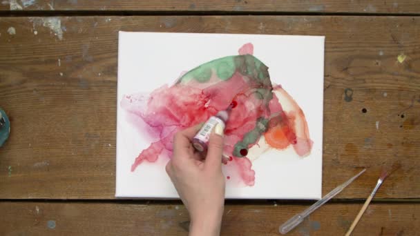 Vista superior da artista feminina pinta um quadro abstrato, ela derrama algumas gotas de dor vermelha para tela molhada e usa pincel para distribuí-lo — Vídeo de Stock