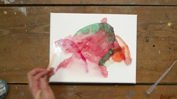 Vista superior do artista masculino pinta um quadro abstrato, ele usa pincel e uma tinta laranja para tintas em tela molhada — Vídeo de Stock