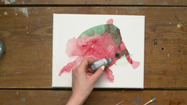 Vista superior da artista feminina pinta um quadro abstrato, ela derrama algumas gotas de dor verde para tela molhada e usa secador para distribuí-lo — Vídeo de Stock