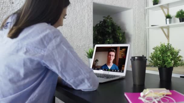 Mujer joven haciendo videollamadas con su médico mientras se queda en casa. Paciente sentado en la mesa de videoconferencia con médico general en el ordenador portátil — Vídeos de Stock