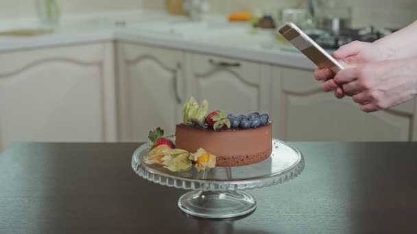 Primer plano de la mujer terminado decorar el pastel de chocolate con bayas y toma una foto de ella — Vídeos de Stock