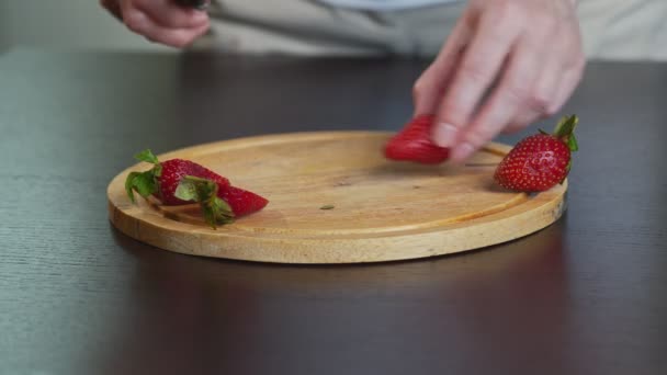 Close-up de uma jovem garota cortando morangos maduros frescos com uma faca em uma tábua de corte de madeira em uma mesa de metal. — Vídeo de Stock