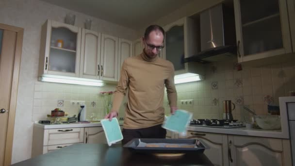 Mann stellt Lebkuchen in Küche in den Ofen — Stockvideo