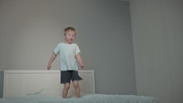 Glücklicher blonder Junge springt nachts zu Hause auf Bett — Stockvideo