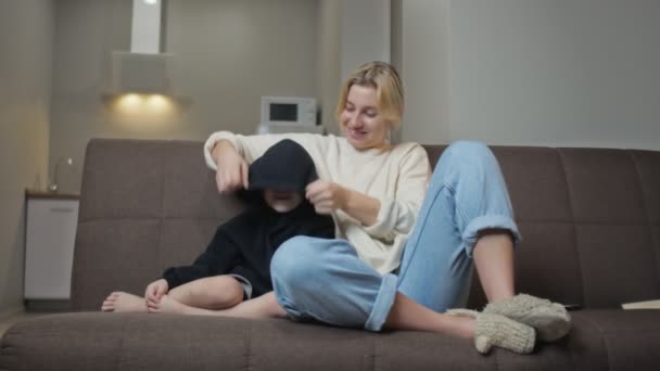 Ung mor sitter med sin son på soffan, tittar på TV och pratar tillsammans — Stockvideo