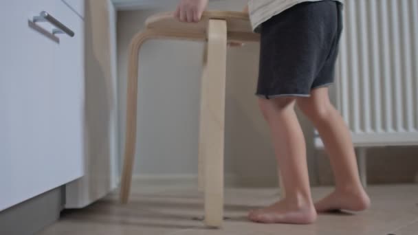 El niño pone un taburete delante del refrigerador, se sube a él y abre el refrigerador. — Vídeos de Stock