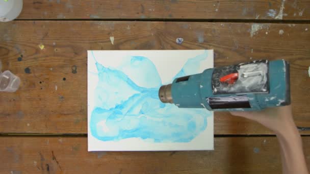 Arte Fluida. Pintura azul abstrata. Vista superior da artista feminina usa secador para secar seu novo quadro — Vídeo de Stock