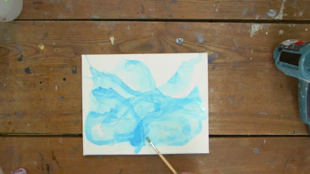 Vista superior do artista pinta um quadro abstrato, ela usa pincel com água em uma imagem azul — Vídeo de Stock