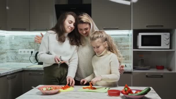 La madre giovane e due le sue figlie cucinano l'insalata a cucina. Madre e le sue figlie tagliano un peperone rosso — Video Stock