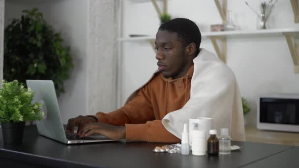 Malade jeune homme afro-américain en utilisant un ordinateur portable à la maison. — Video