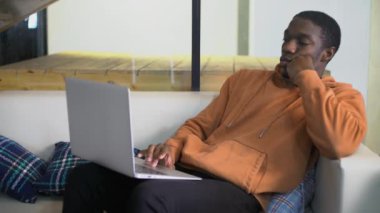 Genç, sıkıcı Afrikalı Amerikalı serbest çalışan öğrenci kanepeye oturur ve defterine bakar.