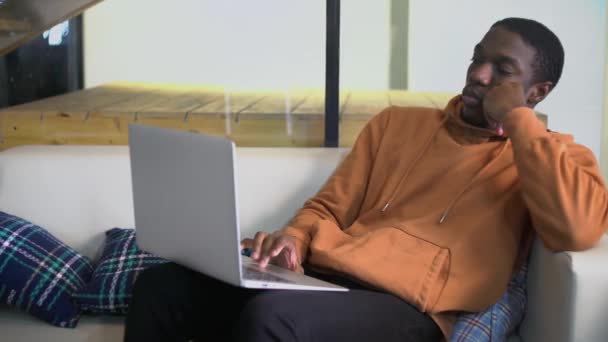 젊은 아프리카 계 미국인 학생 프리랜서가 소파에 앉아서 노트북을 보면서 — 비디오