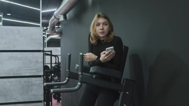 Νεαρή ελκυστική Fitness Γυναίκα χρησιμοποιεί το τηλέφωνο και χαλαρώνει μετά την άσκηση — Αρχείο Βίντεο