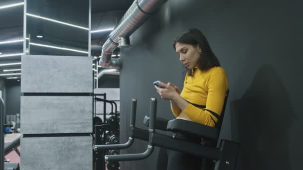 Beatiful Fitness Vrouw in geel topje gebruikt telefoon en ontspant na inspanning — Stockvideo