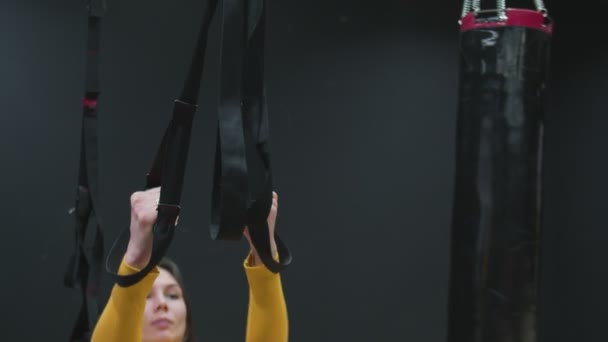 Joven mujer en forma de top amarillo haciendo flexiones con correas de fitness trx en el gimnasio. — Vídeos de Stock