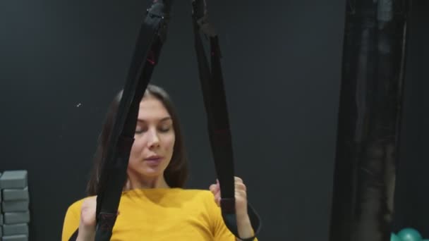 Joven mujer en forma de top amarillo haciendo flexiones con correas de fitness trx en el gimnasio. — Vídeos de Stock