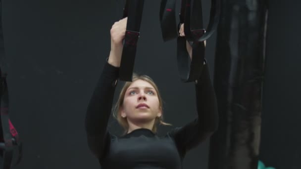 Zmęczona kobieta w czarnym top robi pompki z trx paski fitness w siłowni. — Wideo stockowe