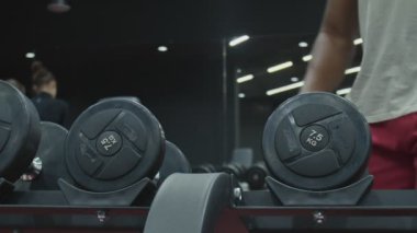 Afrikalı adam spor salonunda bir dambılı alır ve kaldırır.