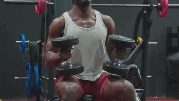 Närbild av muskulös African American Man sitter på bänken och lyfter upp hantlar i gymmet. — Stockvideo