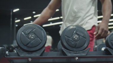 Afrikalı adam spor salonunda iki dambılı alır ve kaldırır.