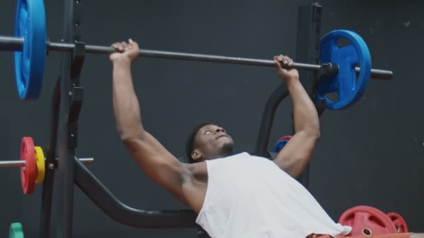 Junger muskulöser Afro-Mann übt Bankdrücken auf der Bank mit der Langhantel — Stockvideo