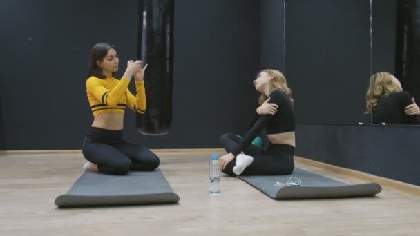 Женщина позирует перед камерой. Две атлетичные женщины расслабляются после тренировки на полу. — стоковое видео