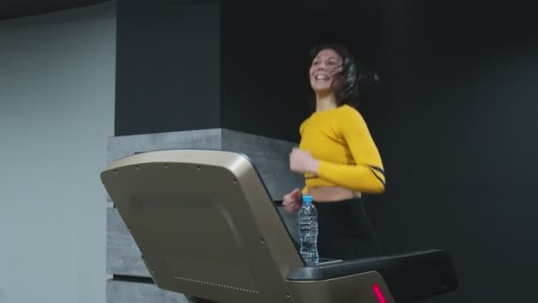 Счастливая молодая женщина в желтом топе бегает по беговой дорожке и спортзалу. — стоковое видео