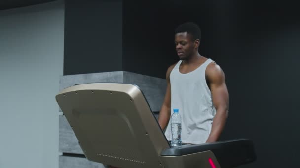 Muskulös afro-amerikansk man går på löpband för att värma upp innan träning — Stockvideo