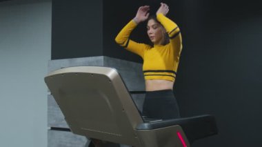 Spor salonunda koşu bandında yürürken spor yapan kadın ısınmak için egzersiz yapıyor.