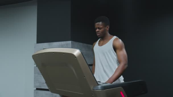 Muskulös afro-amerikansk man går på löpband och använder telefon i gymmet — Stockvideo