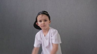 Beyaz tişörtlü ve siyah şapkalı küçük çocuk elleri ile breakdance hip-hop yapıyor..