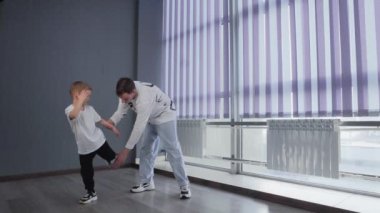 Beyaz tişörtlü küçük çocuk öğretmeniyle break dans yapıyor.