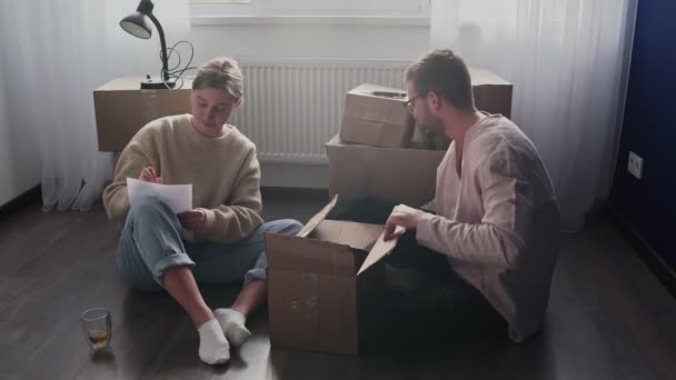 Glückliches Paar packt Kartons, bereitet sich auf den Umzug vor, Familie sitzt am Umzugstag auf dem Fußboden im Wohnzimmer — Stockvideo