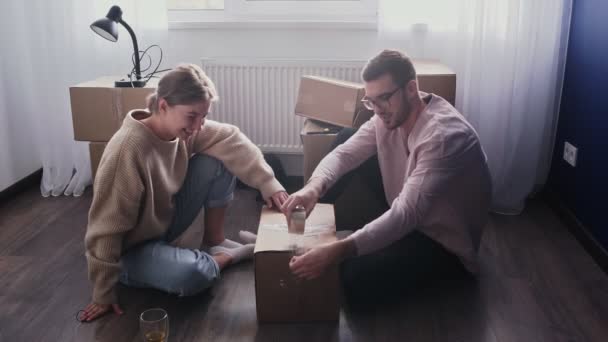 Glückliches Paar packt Kartons, bereitet sich auf den Umzug vor, Familie sitzt am Umzugstag auf dem Fußboden im Wohnzimmer — Stockvideo