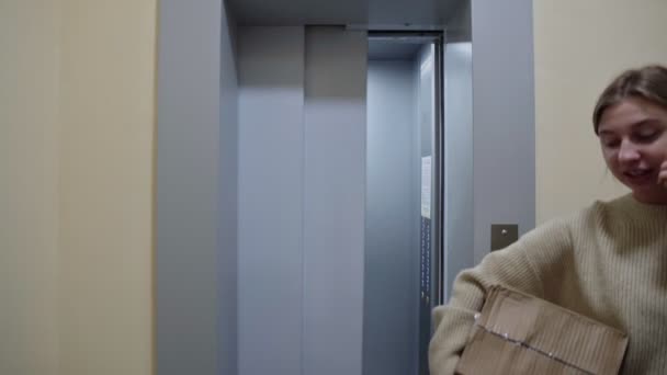 Νεαρή γυναίκα εισέρχεται στο ασανσέρ με κουτιά από χαρτόνι και πτυσσόμενη καρέκλα κινείται σε νέο διαμέρισμα — Αρχείο Βίντεο